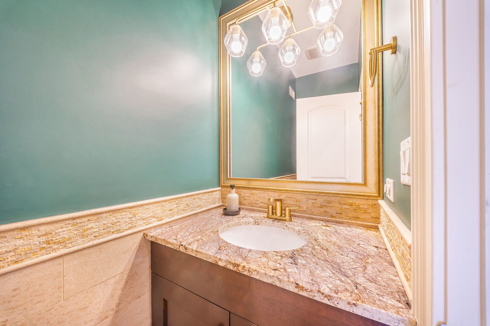 Bathroom vanity with a veined stone counter, oval sink, and gold-framed mirror against teal walls.