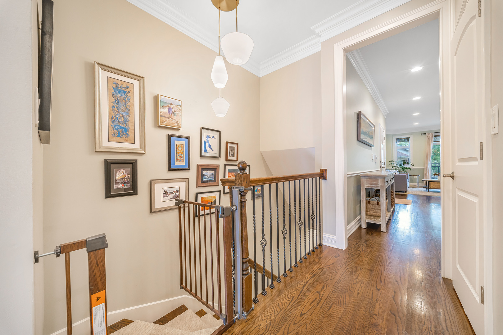 Stair landing with hardwood floors, metal railings, a gallery wall, and an open doorway to the living area.