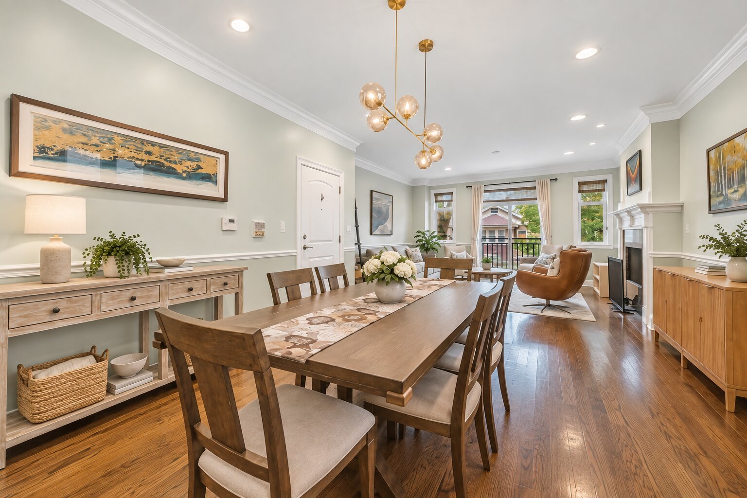 Dining room with a long wood table, hardwood floors, and adjoining fireplace seating area.