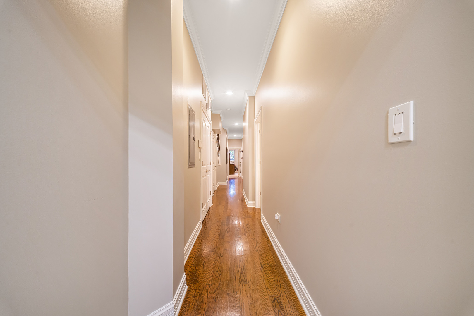 Apartment hallway with polished hardwood floors, beige walls, and recessed ceiling lights.
