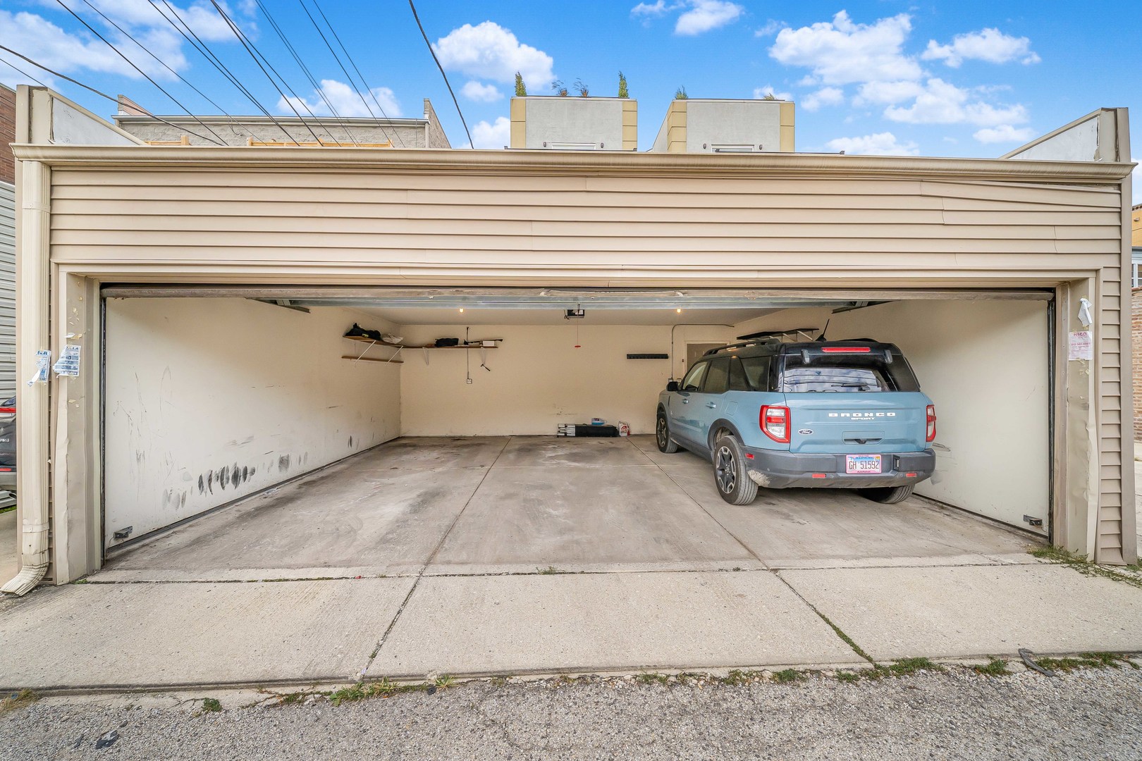 Open two-car garage with a blue Bronco parked on the right and storage shelves along the back wall.