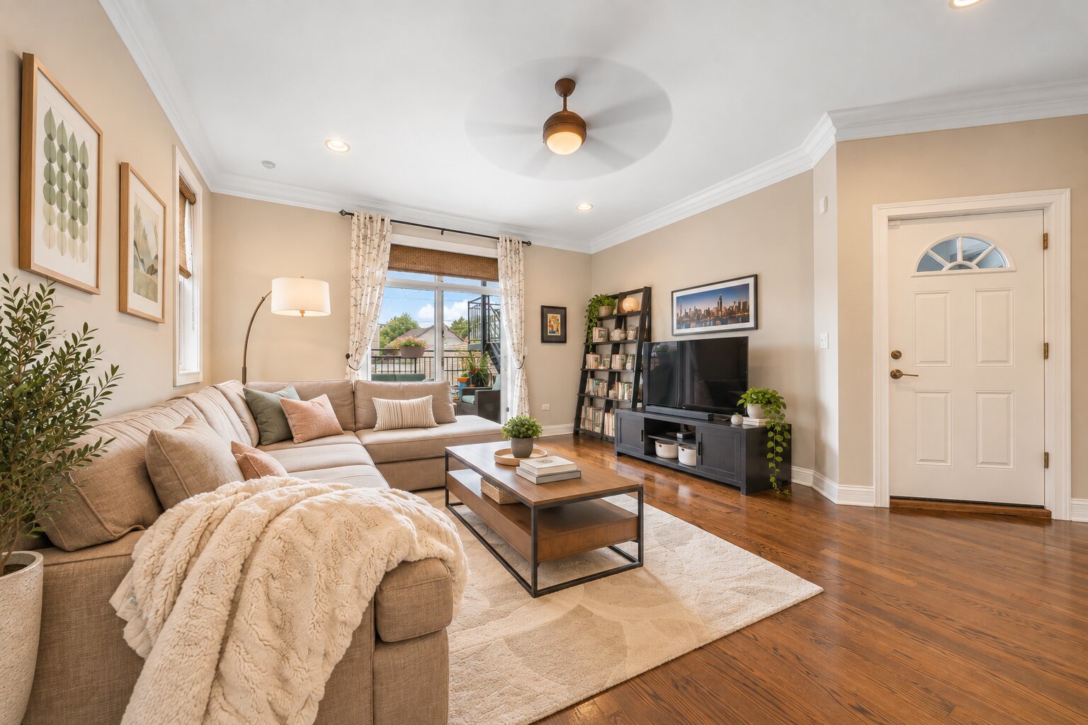 Staged living room with a beige sectional, hardwood floors, and sliding doors to a balcony.