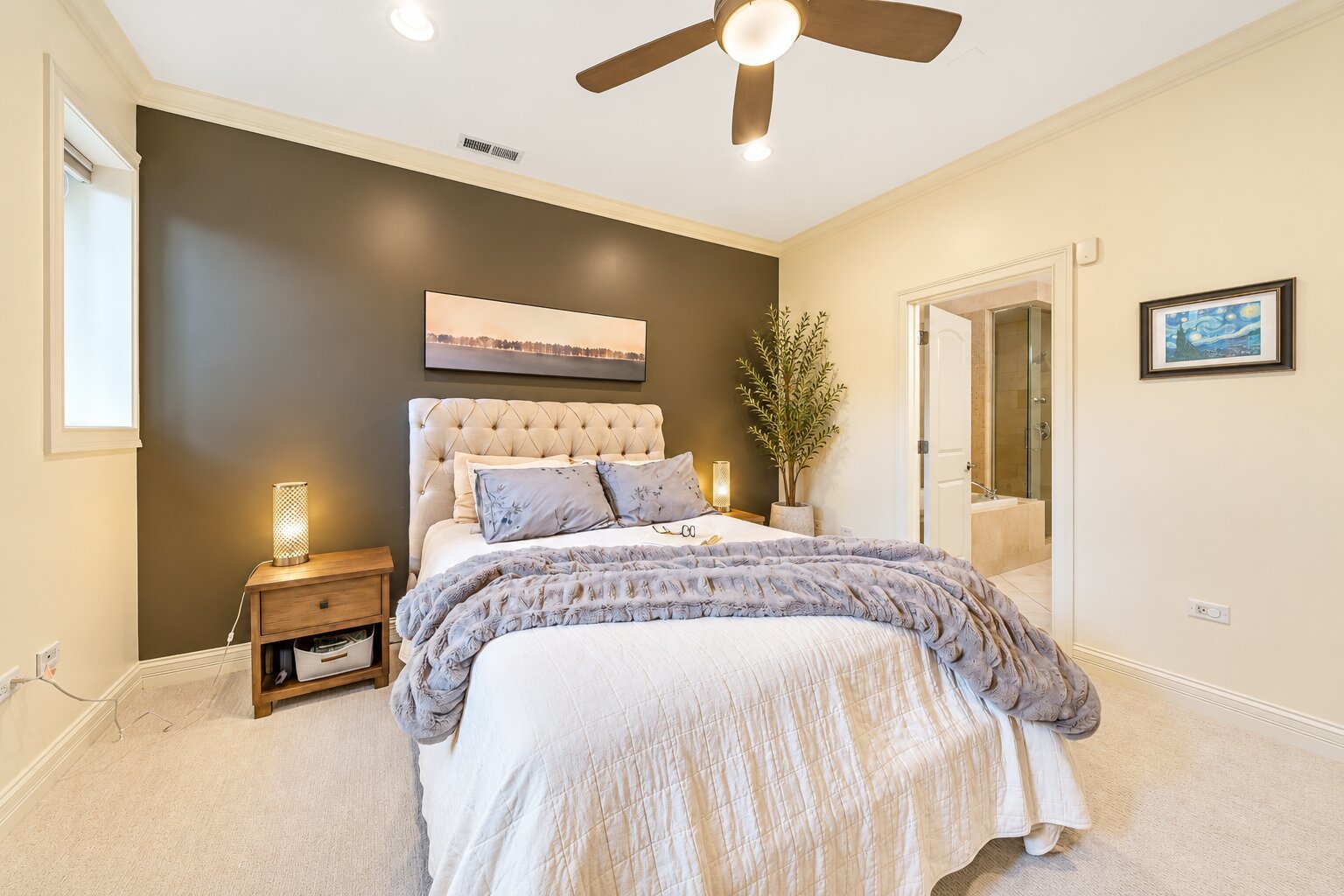 Bedroom with a white tufted bed against a charcoal accent wall and an ensuite bathroom doorway.