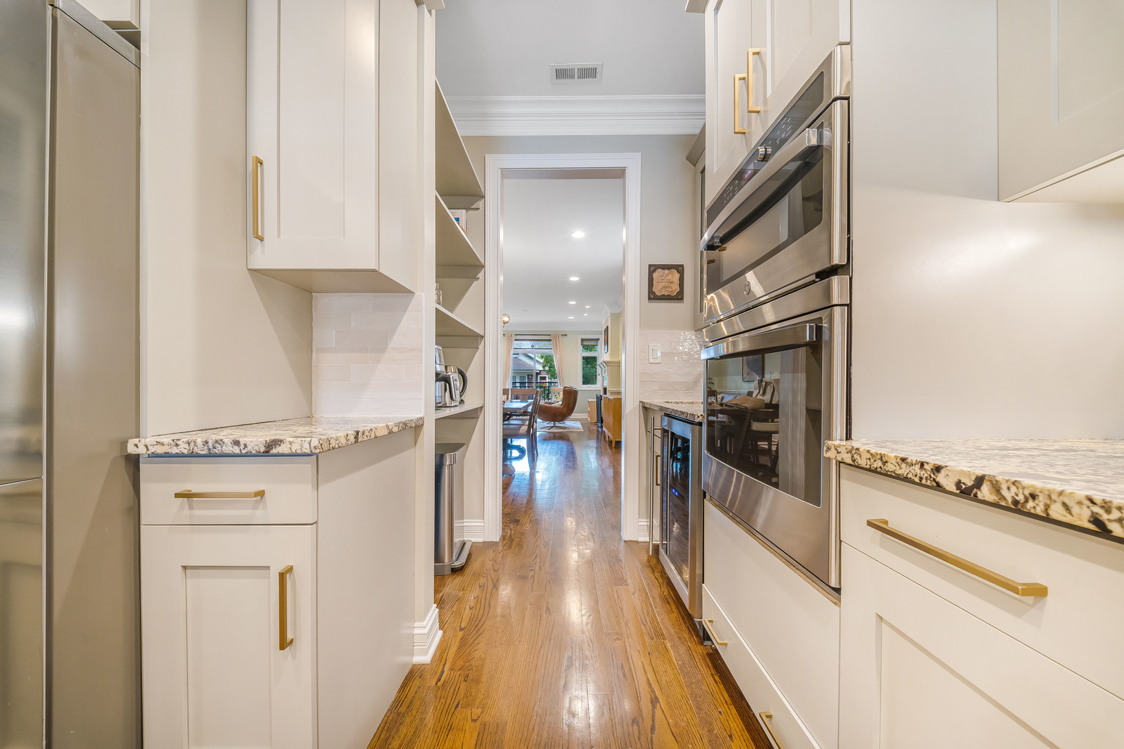 Renovated galley kitchen with white cabinets, brass hardware, stainless steel appliances, and hardwood floors.
