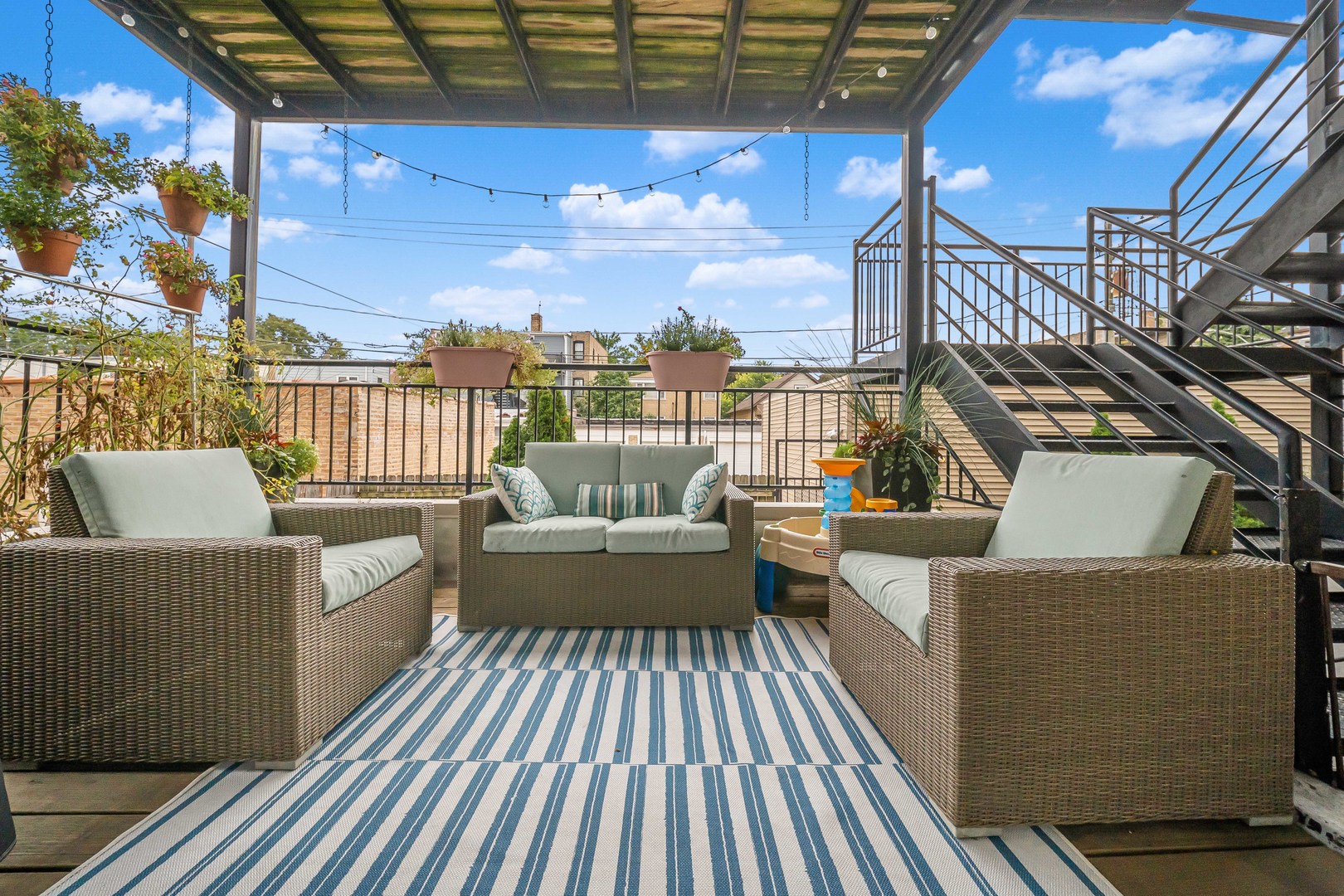 Rooftop deck with wicker seating, a striped rug, potted plants, and a wood pergola.
