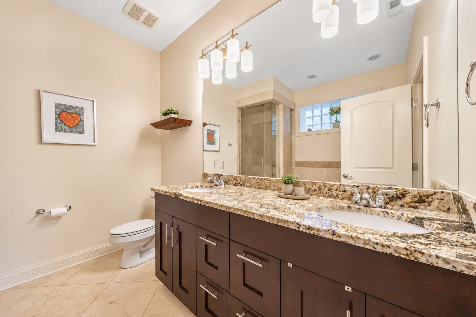 Bathroom with a dark double vanity, patterned stone countertop, and glass-enclosed shower.