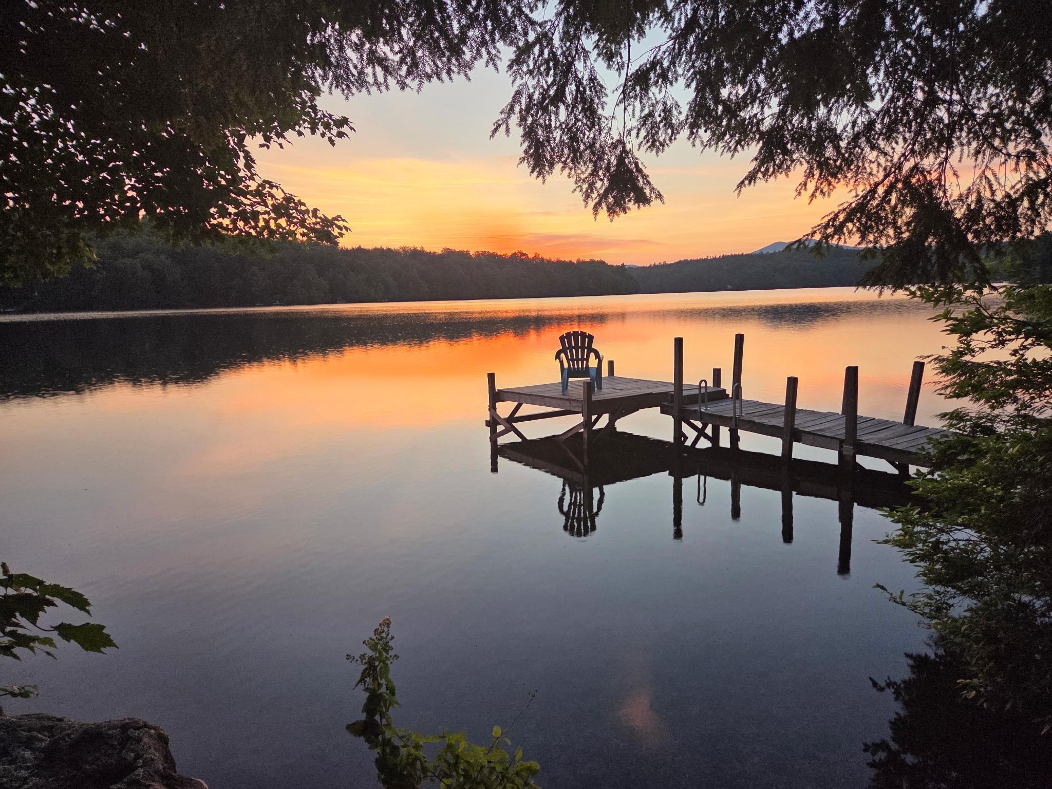Wooden dock and Adirondack chair over a calm lake at sunset