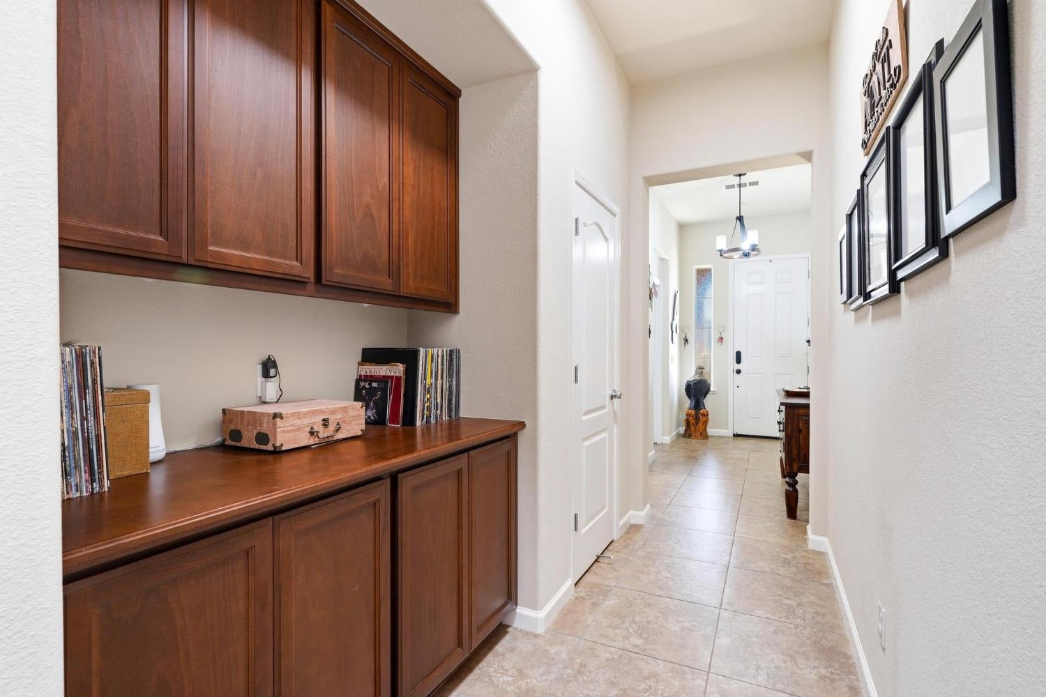 Hallway with dark wood built-in cabinets, framed wall art, and tile flooring leading to the front door.