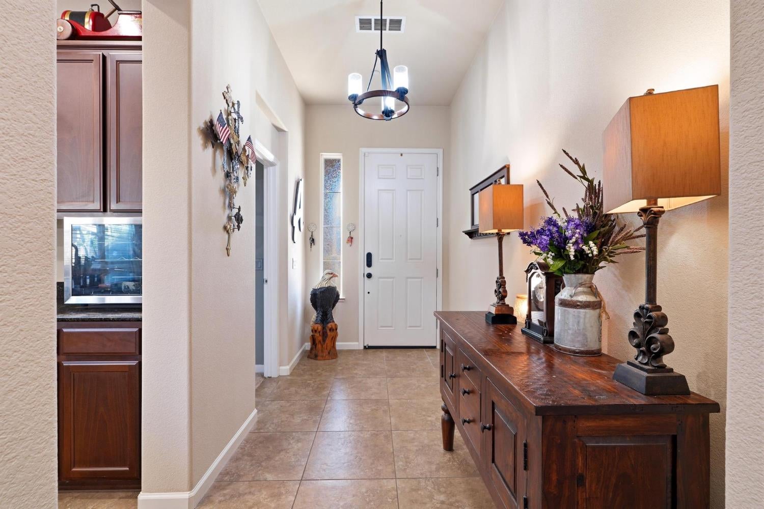 Entry foyer with tiled floors, a white front door, and a dark wood console decorated with flowers and lamps.