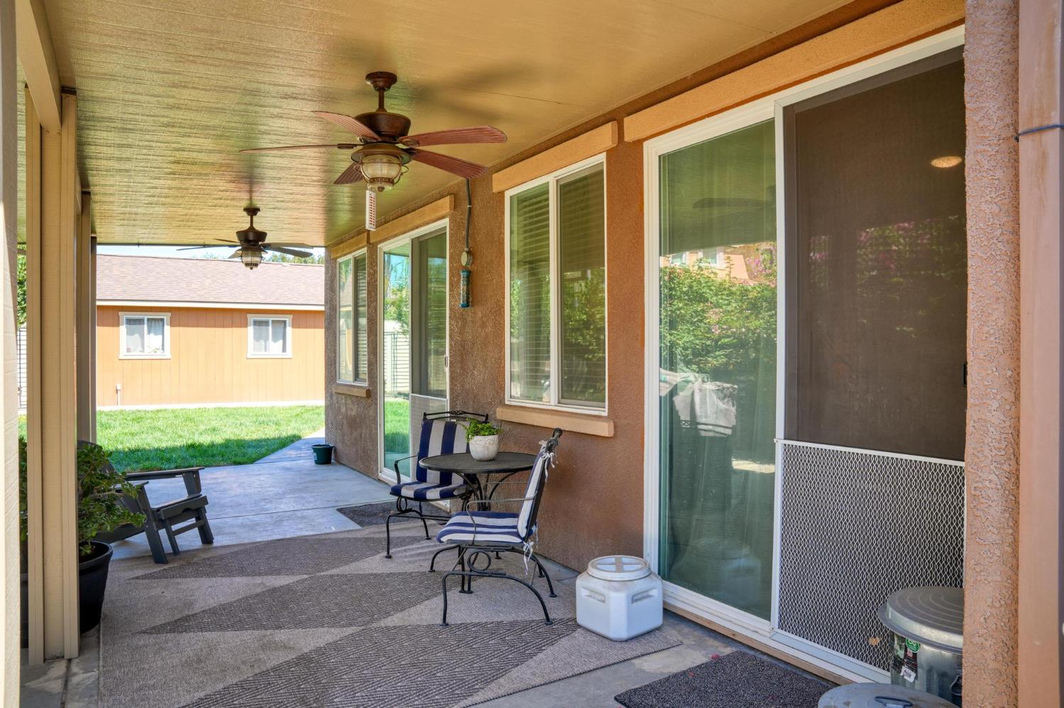 Covered backyard patio with ceiling fans, striped seating, and sliding glass doors.