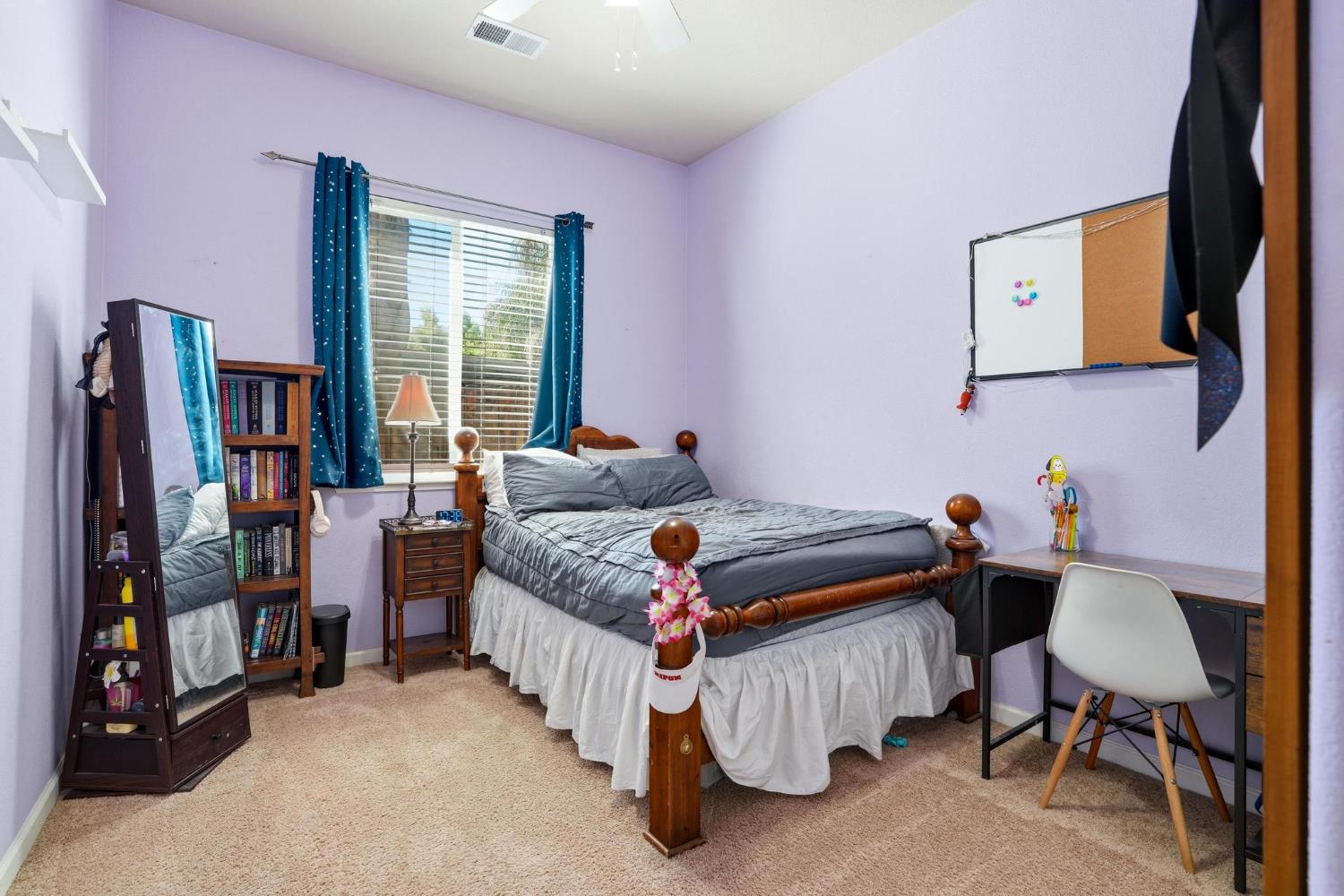 Bedroom with a wooden bed, gray bedding, blue curtains, and a desk with whiteboard.