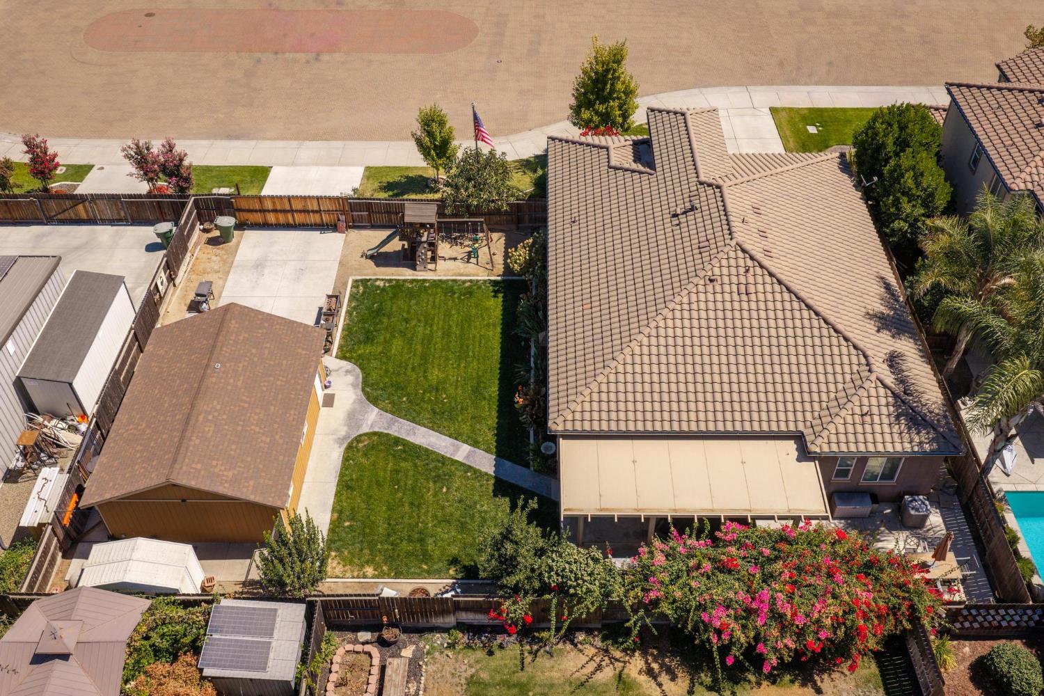 Fenced backyard with a large lawn, concrete patio, detached shed, and play area.