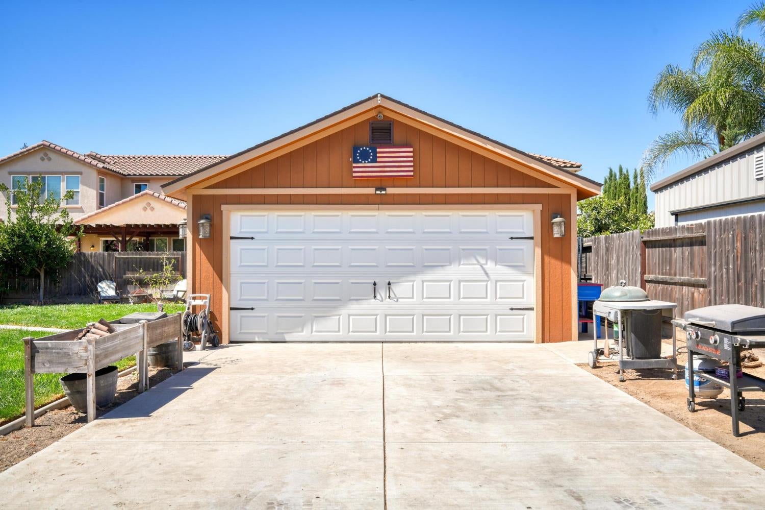 Detached orange-brown garage with a white double door and flag above a broad concrete driveway.