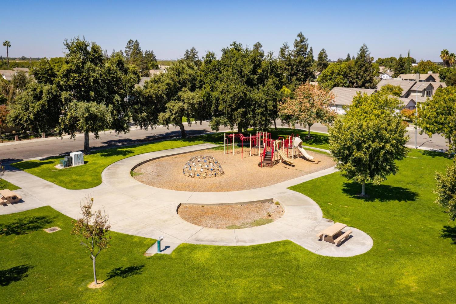 Neighborhood park with a playground, climbing dome, curved paths, and surrounding lawns.