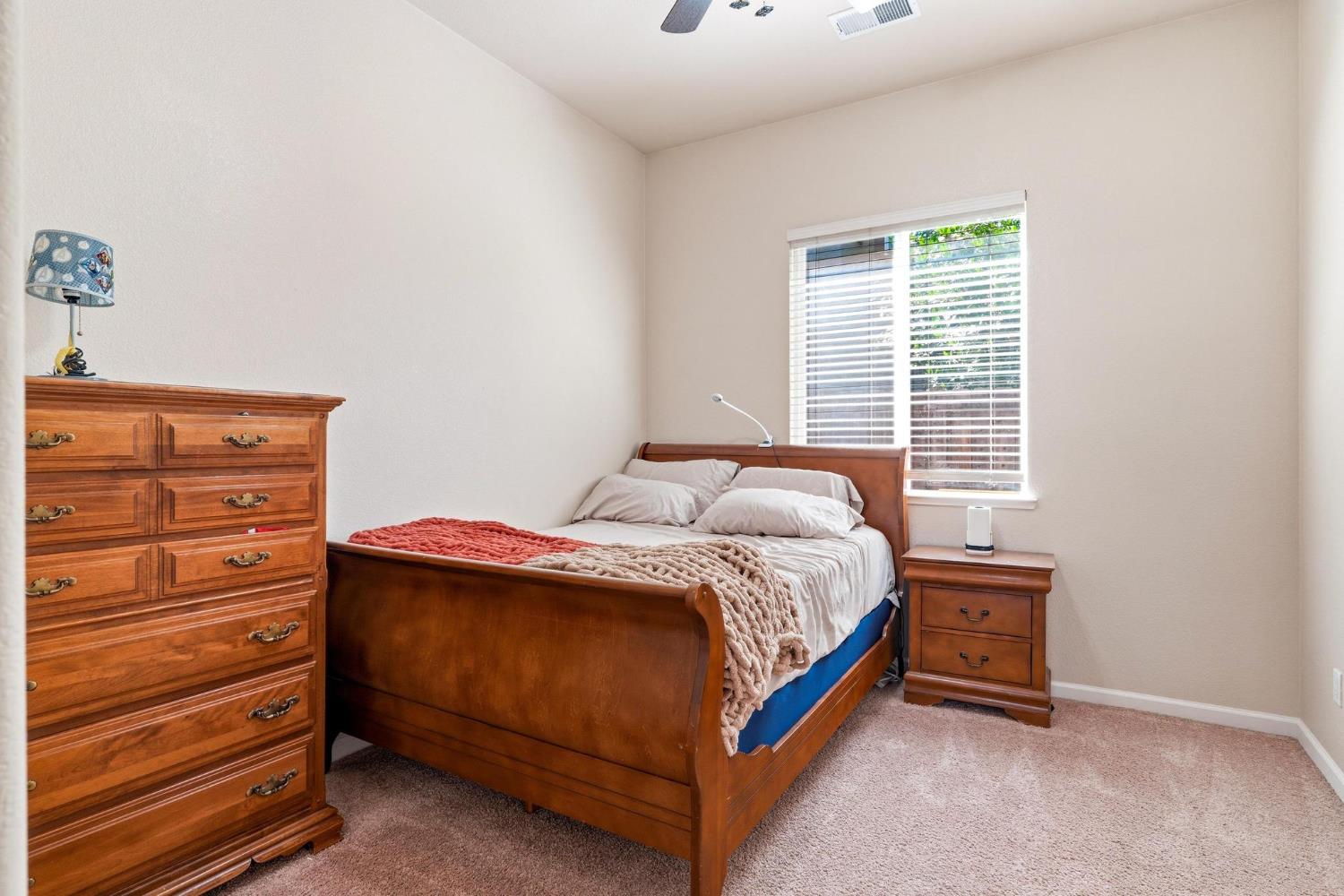 Bedroom with wooden bed and matching furniture beside a window with blinds.