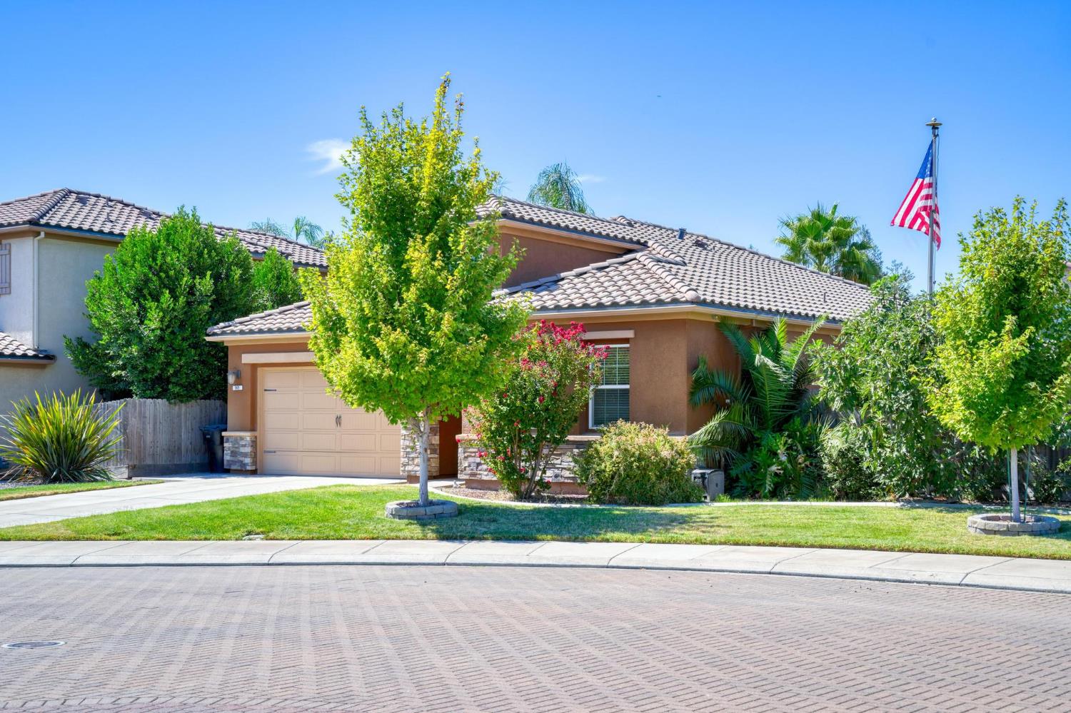 Single-story stucco home with a tile roof, landscaped front yard, and American flag.