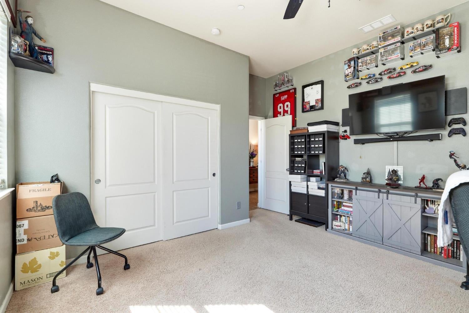 Bedroom with white closet doors, a wall-mounted TV, and shelves displaying sports memorabilia and collectibles.