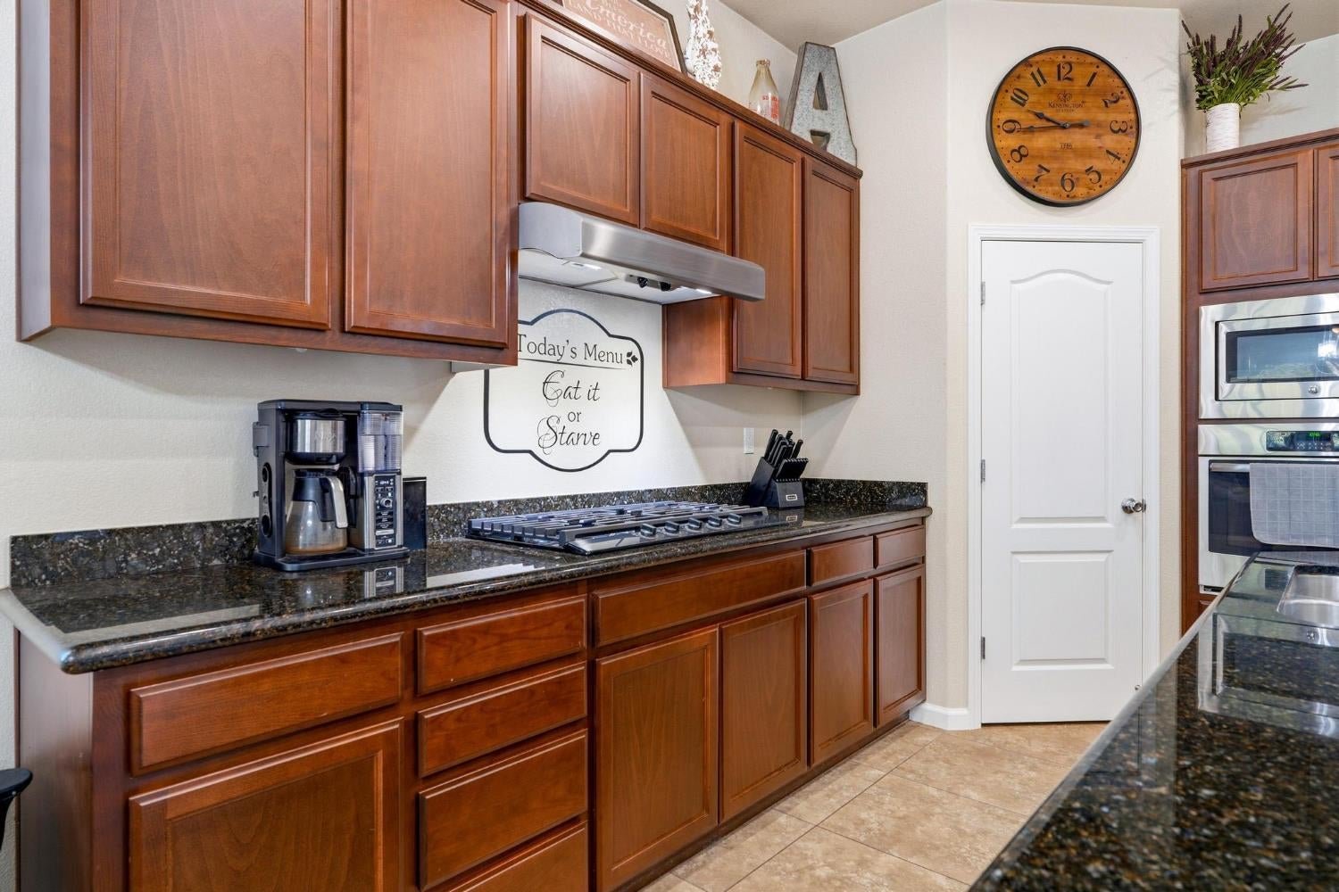 Kitchen with reddish-brown cabinets, dark granite counters, a gas cooktop, and stacked double ovens.