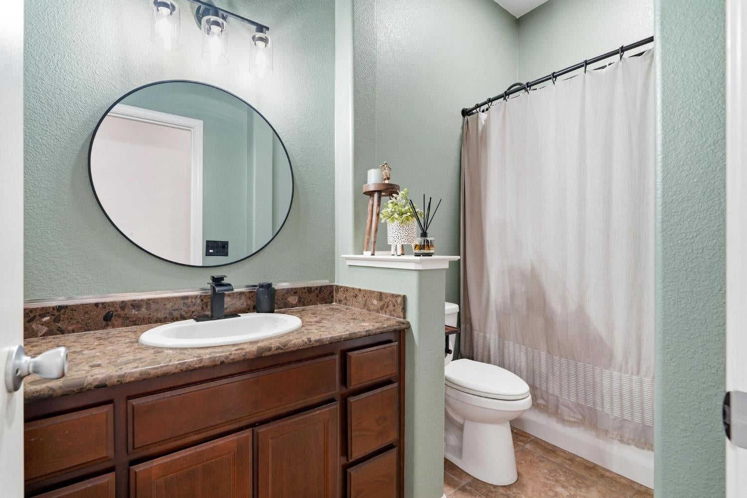 Bathroom with a dark wood vanity, brown stone counter, oval mirror, and curtained tub or shower.