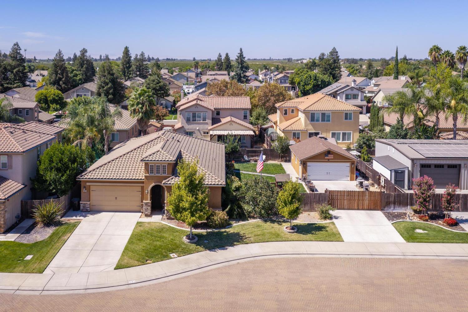 Two-story tan house with a tile roof and landscaped yard, seen from above among neighboring homes.