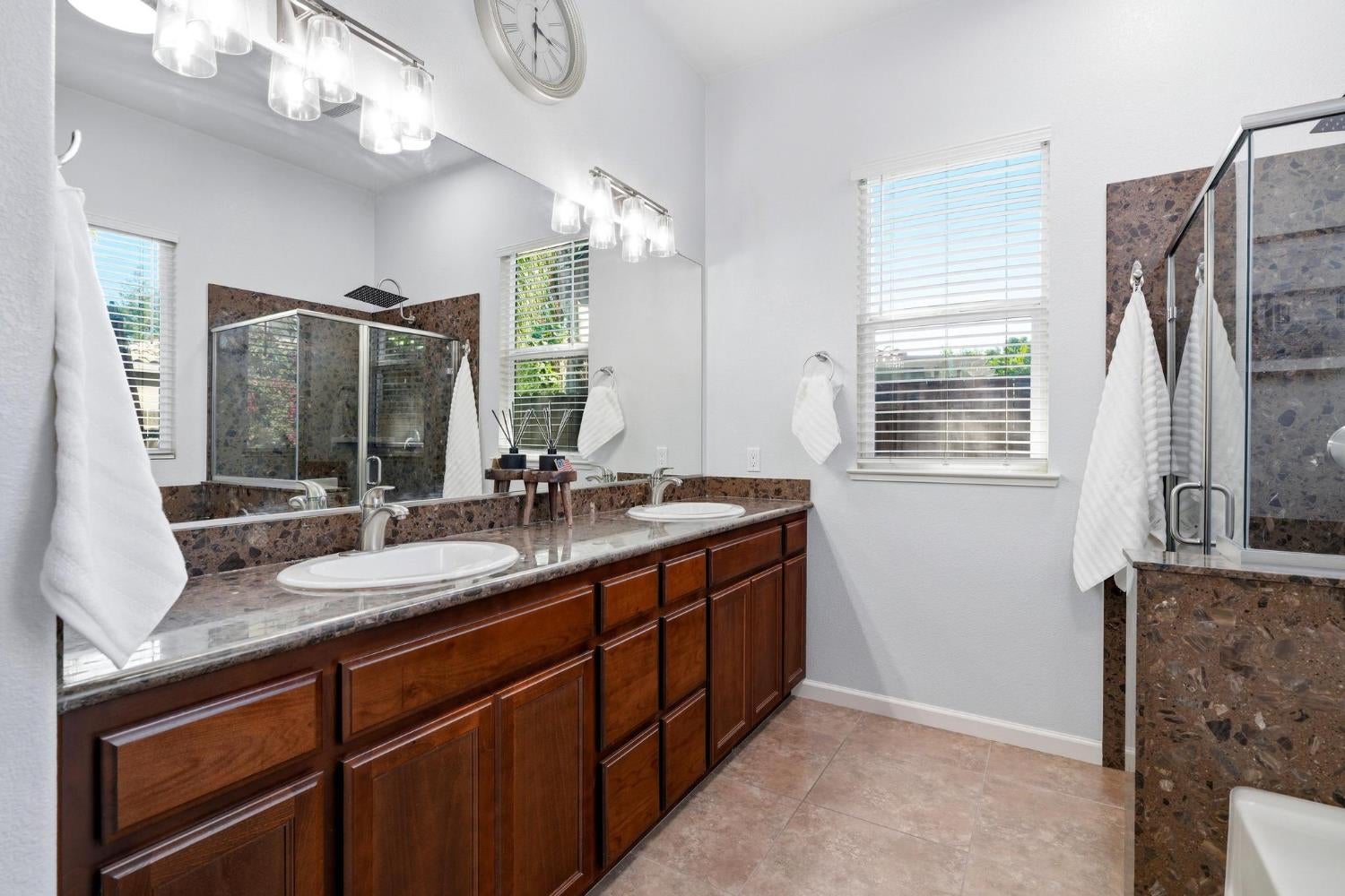 Bright bathroom with a double-sink vanity, dark wood cabinets, and a glass-enclosed shower.