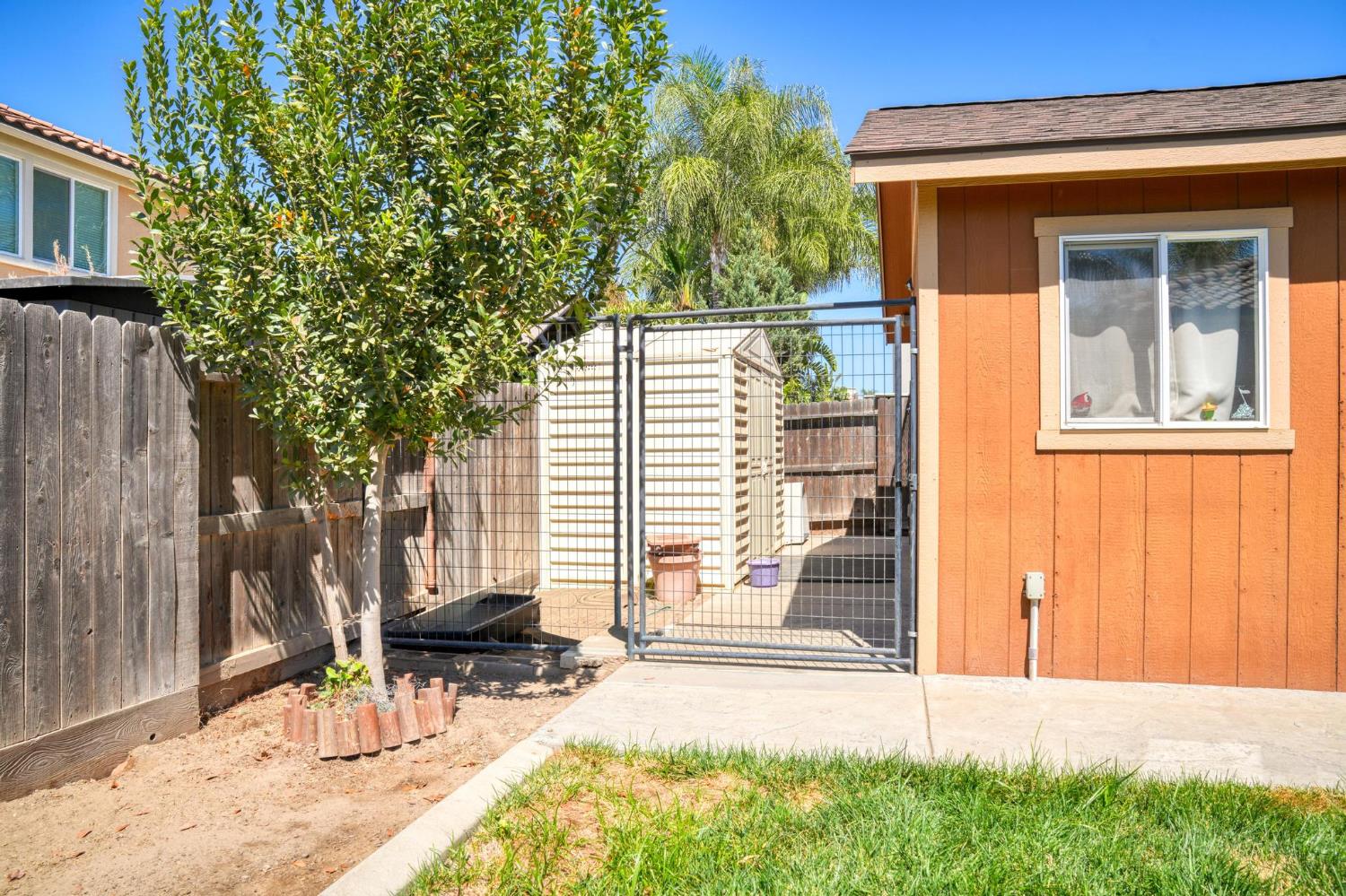 Backyard with a metal gate, orange outbuilding, wooden fence, and small lawn.