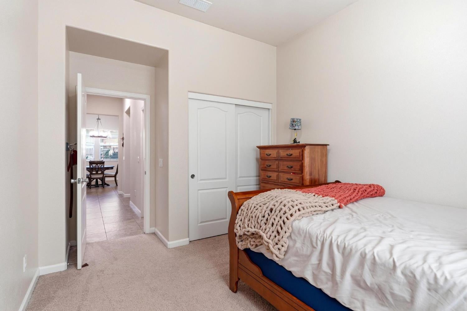 Bedroom with a wooden bed, coral and cream throws, dresser, and sliding closet doors.