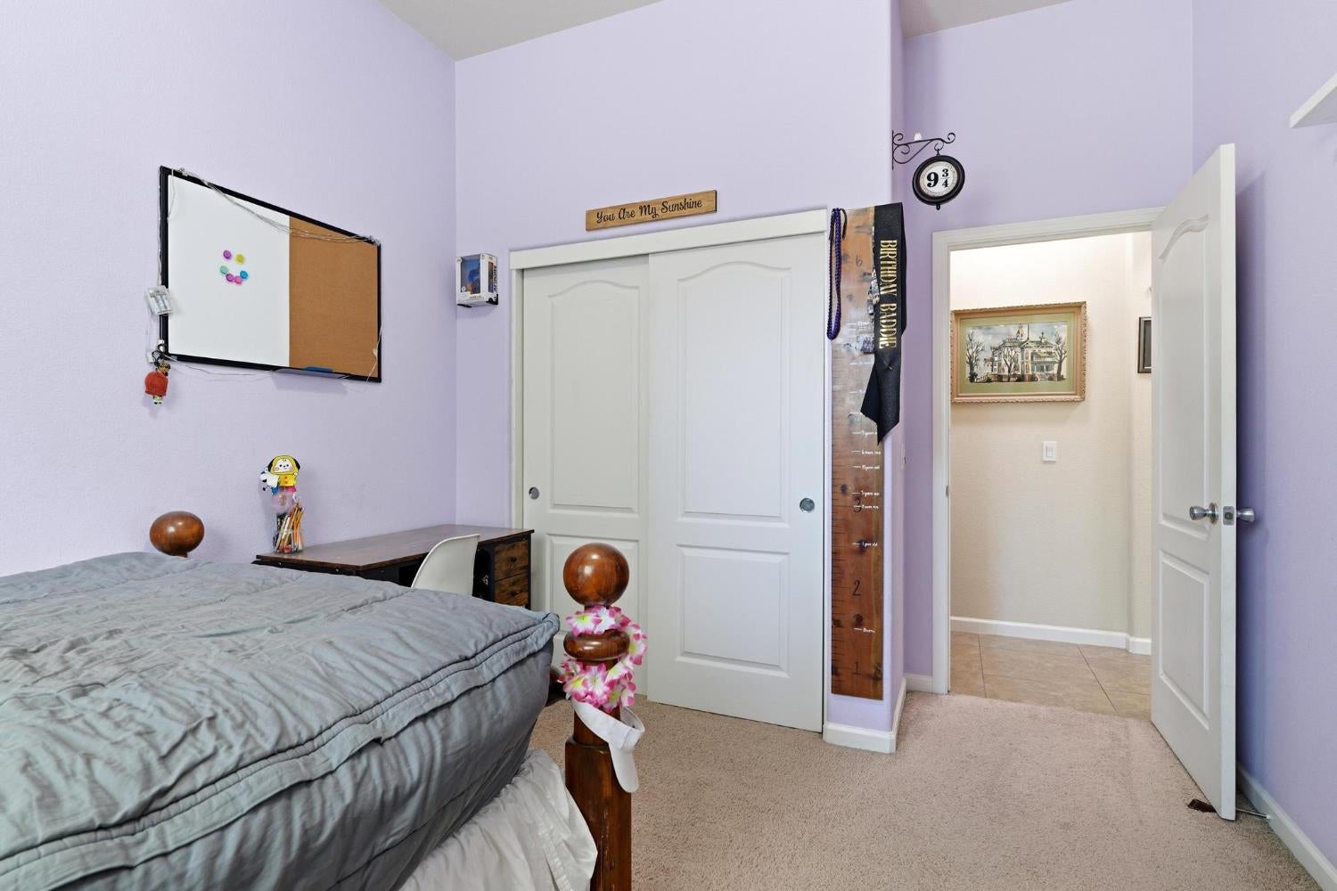 Bedroom with lavender walls, a gray bed, and white sliding closet doors beside an open doorway.