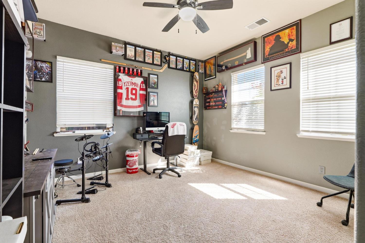 Home office with a computer desk, electronic drum kit, and hockey memorabilia displayed on the walls.