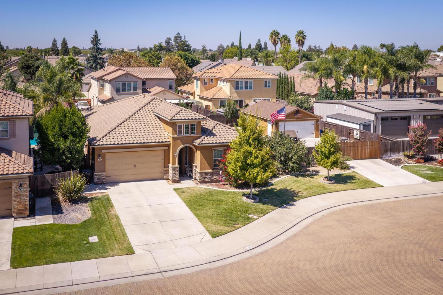 Aerial view of a tan two-story home with a tiled roof, broad driveway, and green front lawn.