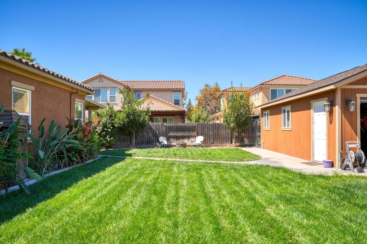 Backyard with a broad green lawn, patio seating, and a wooden outbuilding.