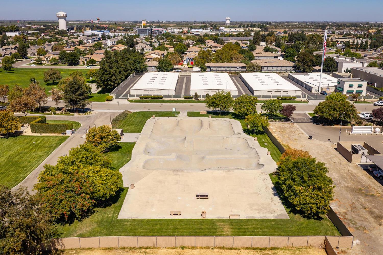 Aerial view of a concrete skate park with ramps and bowls, surrounded by lawns and trees.