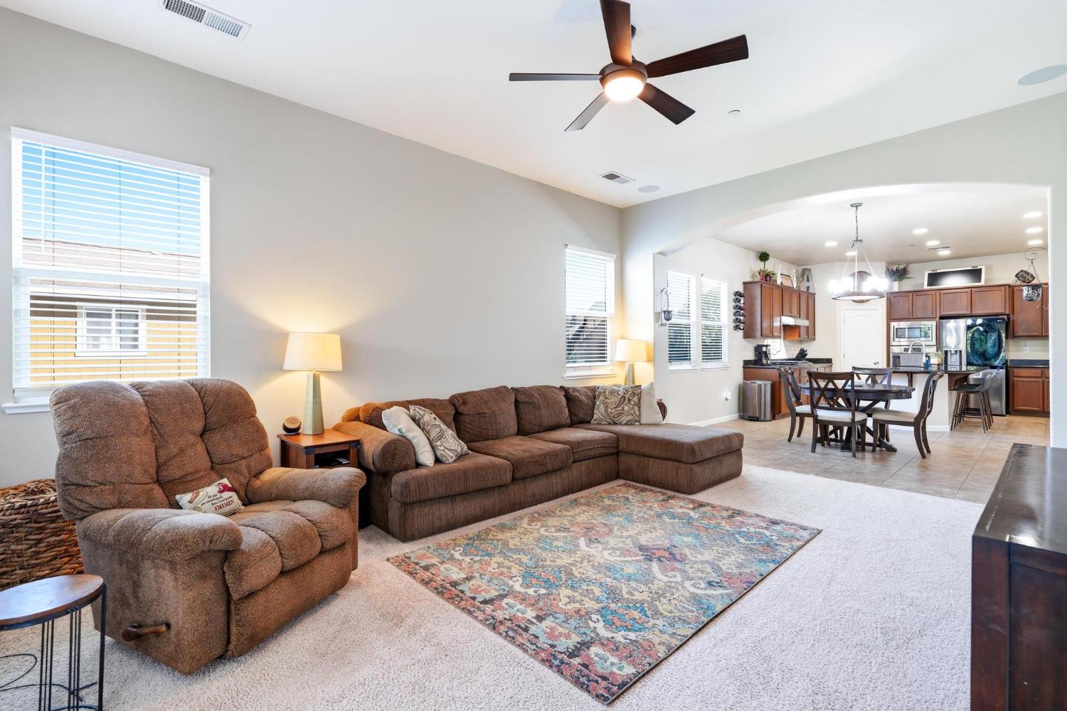 Furnished living room with brown sectional and recliner opening to a dining area and kitchen.