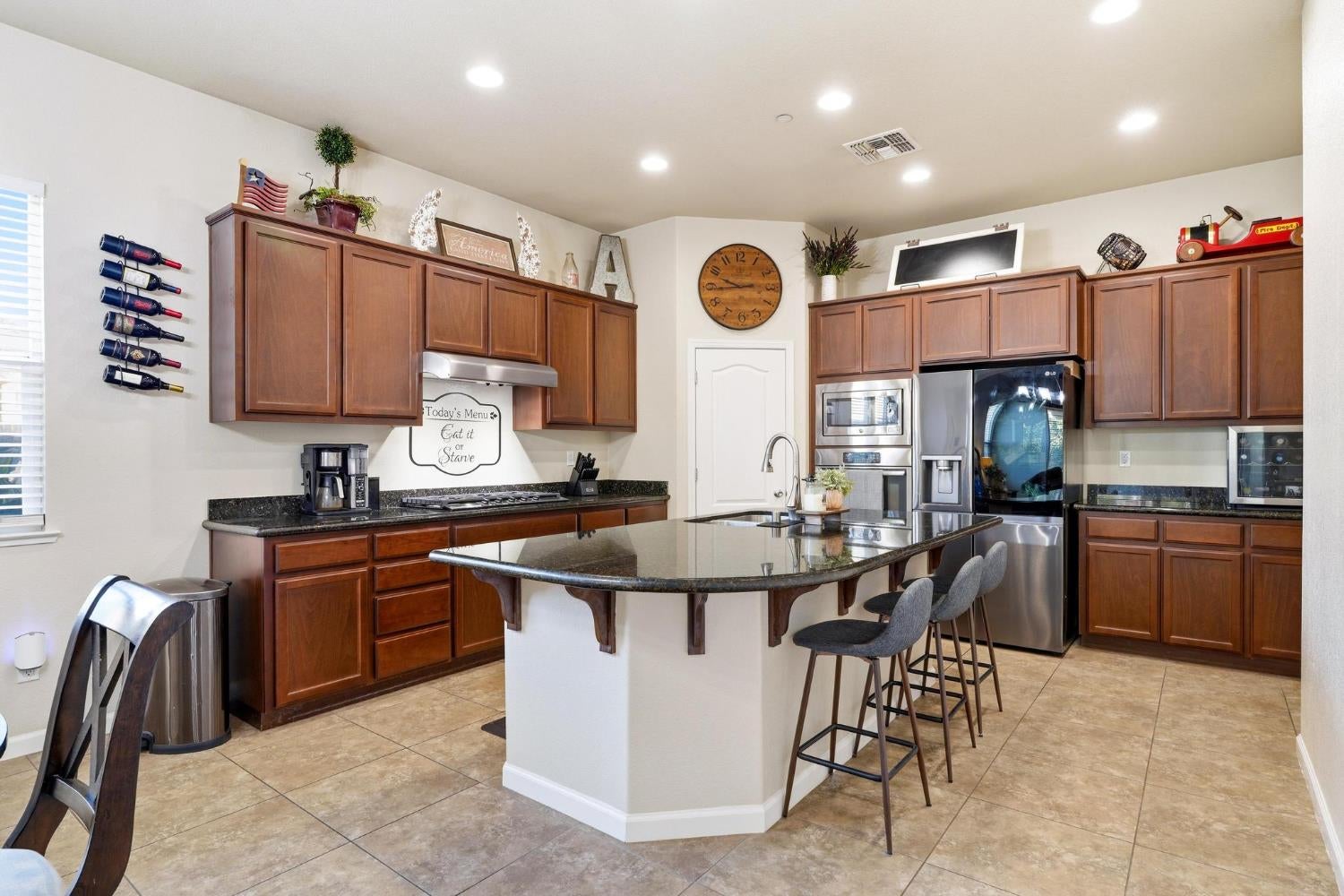 Kitchen with dark wood cabinetry, granite island, bar stools, and stainless steel appliances.