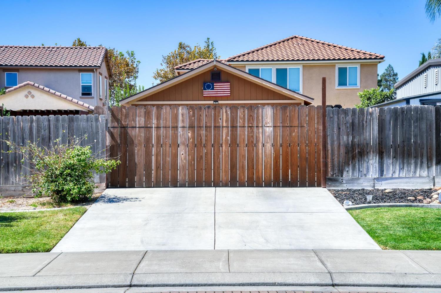 House behind a tall wooden fence and gate, with a concrete driveway and tiled roof.