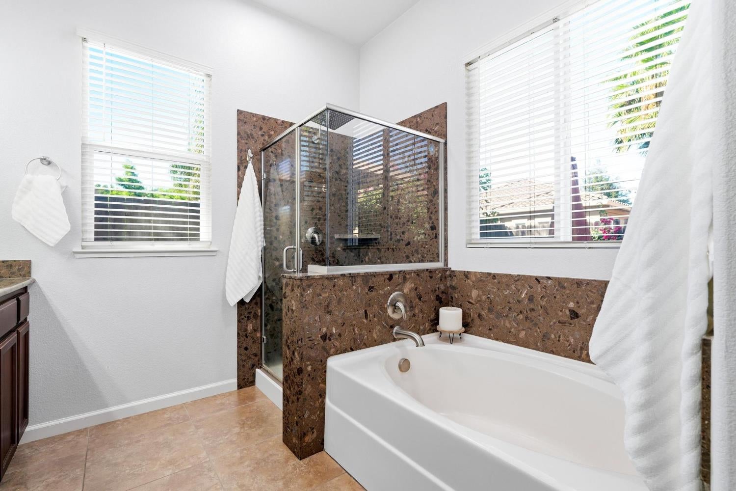 Bathroom with a white soaking tub, glass-enclosed shower, and brown stone-look tile.