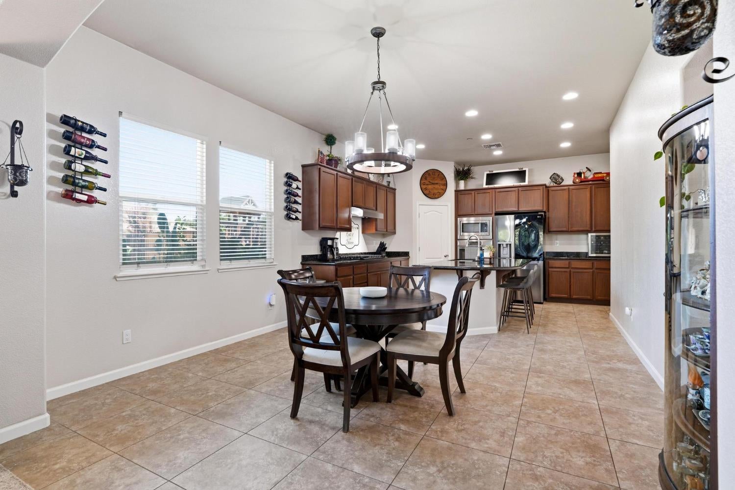 Dining area opening into a kitchen with dark wood cabinets, stainless steel appliances, and tan tile floors.