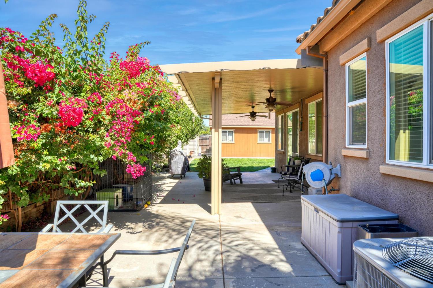 Covered backyard patio with a hot tub, ceiling fans, and vivid pink flowering vines.