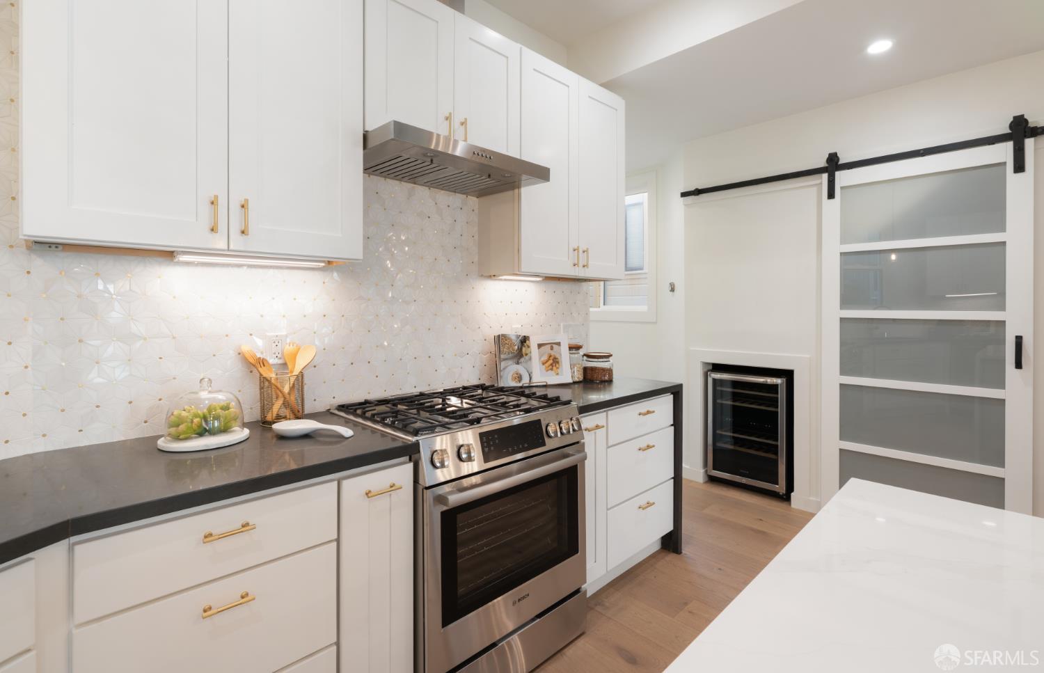 Kitchen with white shaker cabinets, geometric tile backsplash, stainless steel range, and glass-front wine refrigerator.