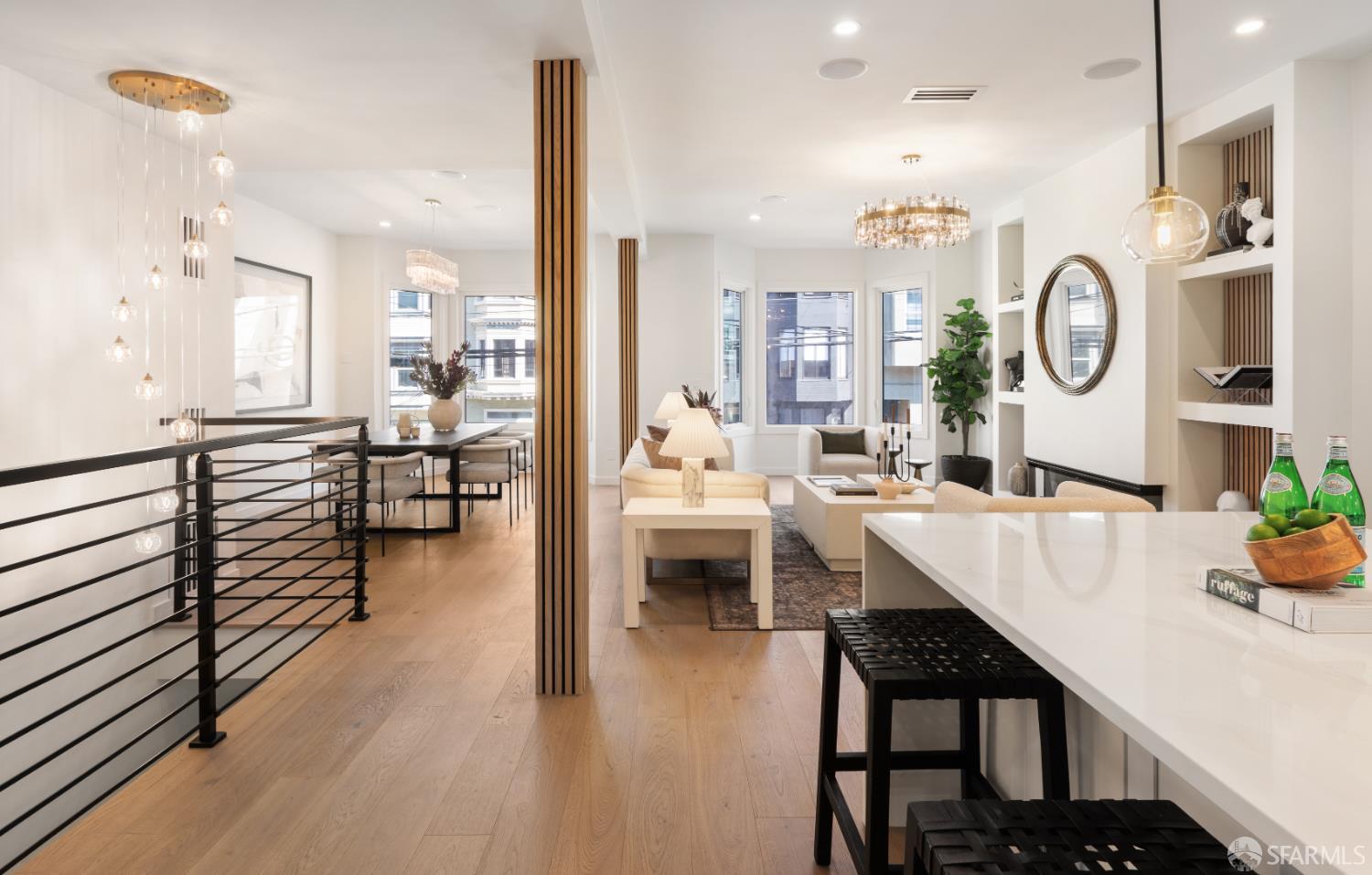 Open-plan living, dining, and kitchen area with pale wood floors, white island, and large windows.