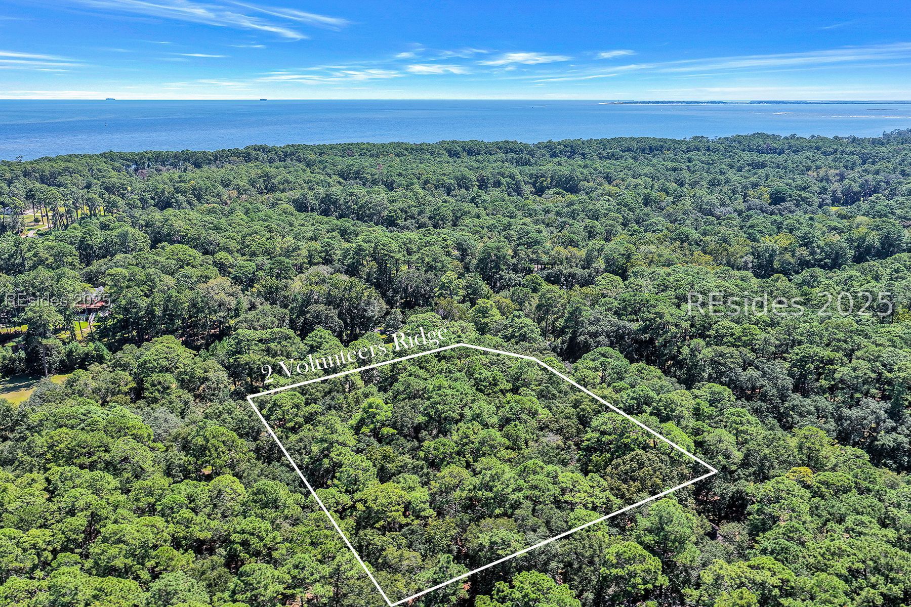 Aerial view of the wooded 2 Volunteers Ridge parcel, outlined in white, with water beyond.