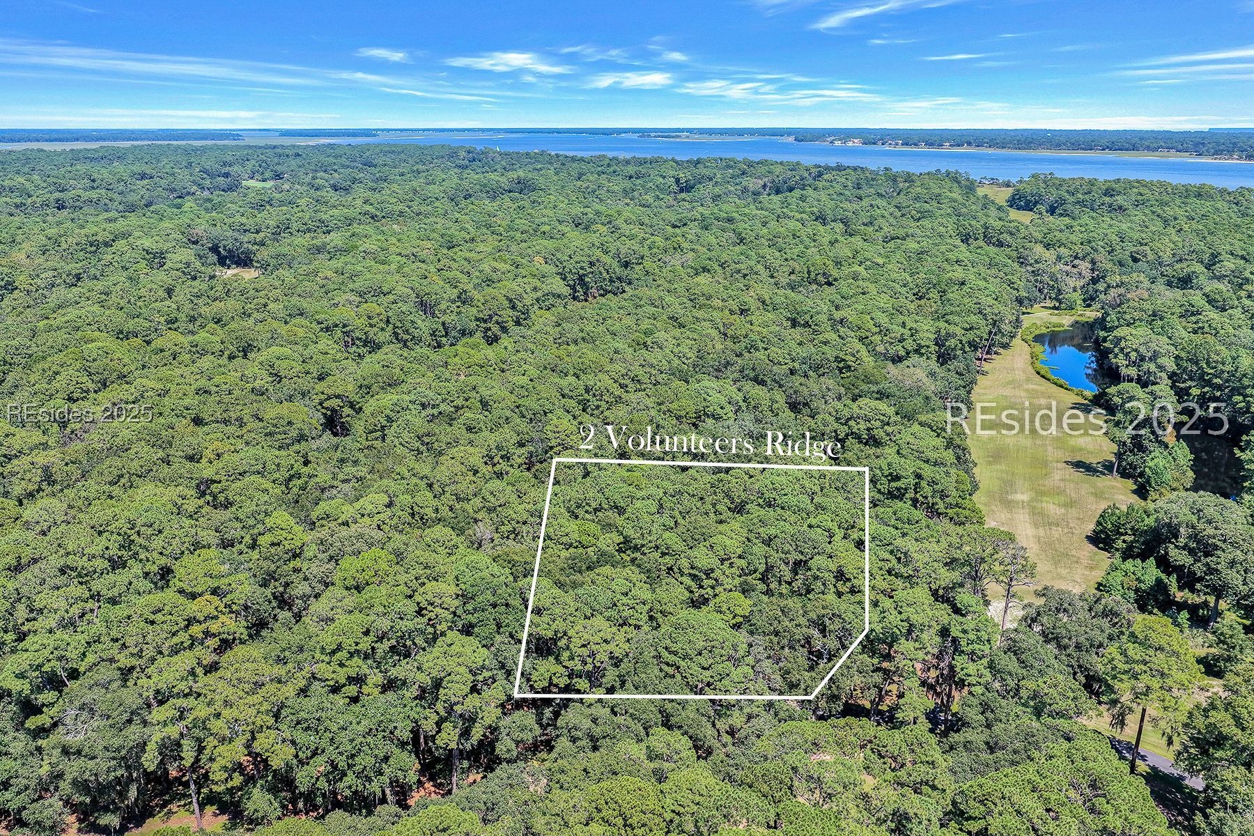 Aerial view of the wooded 2 Volunteers Ridge parcel outlined in white, with a pond and distant waterway.