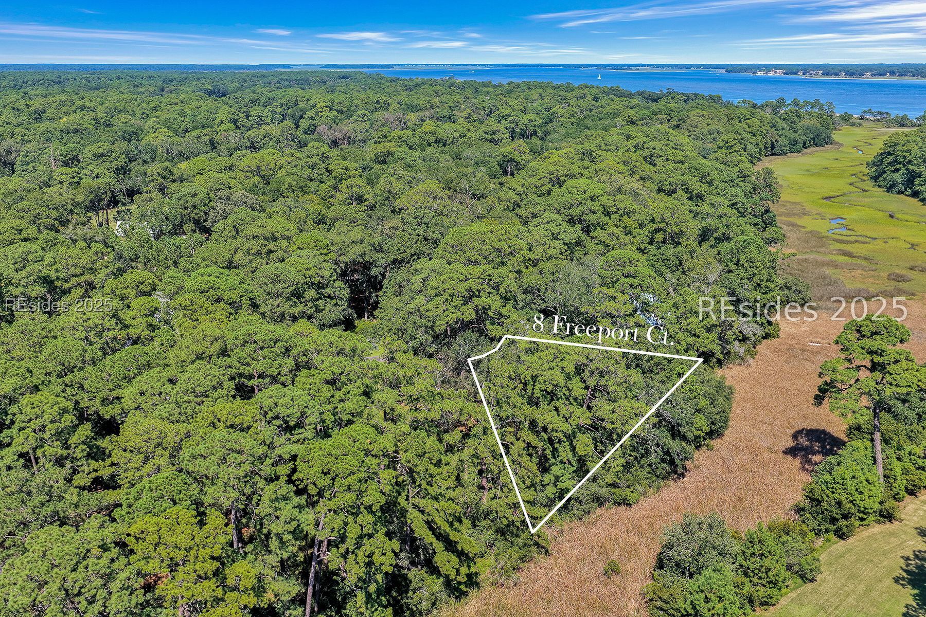 Aerial view of wooded 8 Freeport Court lot outlined beside marsh, with water in the distance.