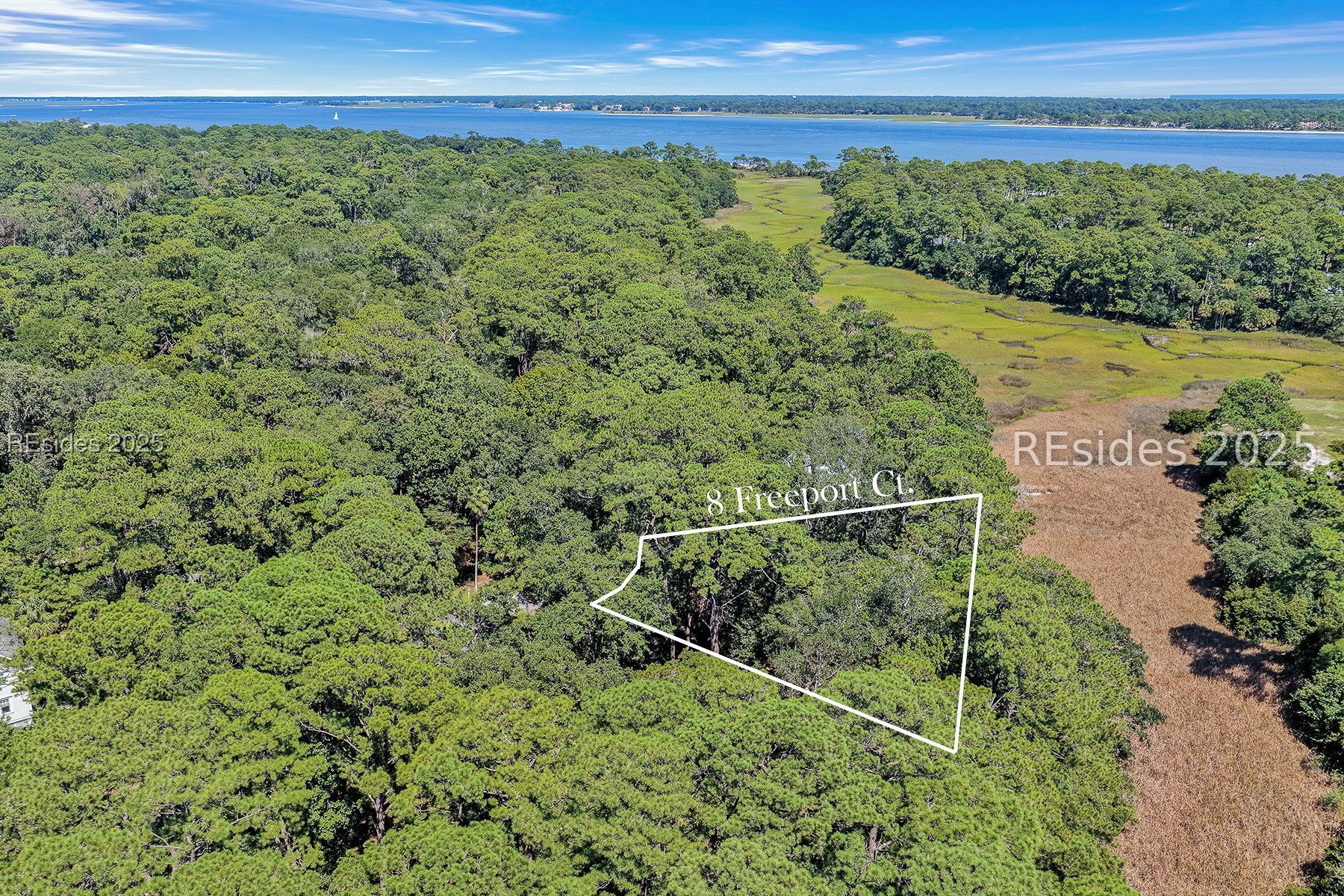Aerial view of the wooded 8 Freeport Court lot outlined beside marsh, with water beyond.