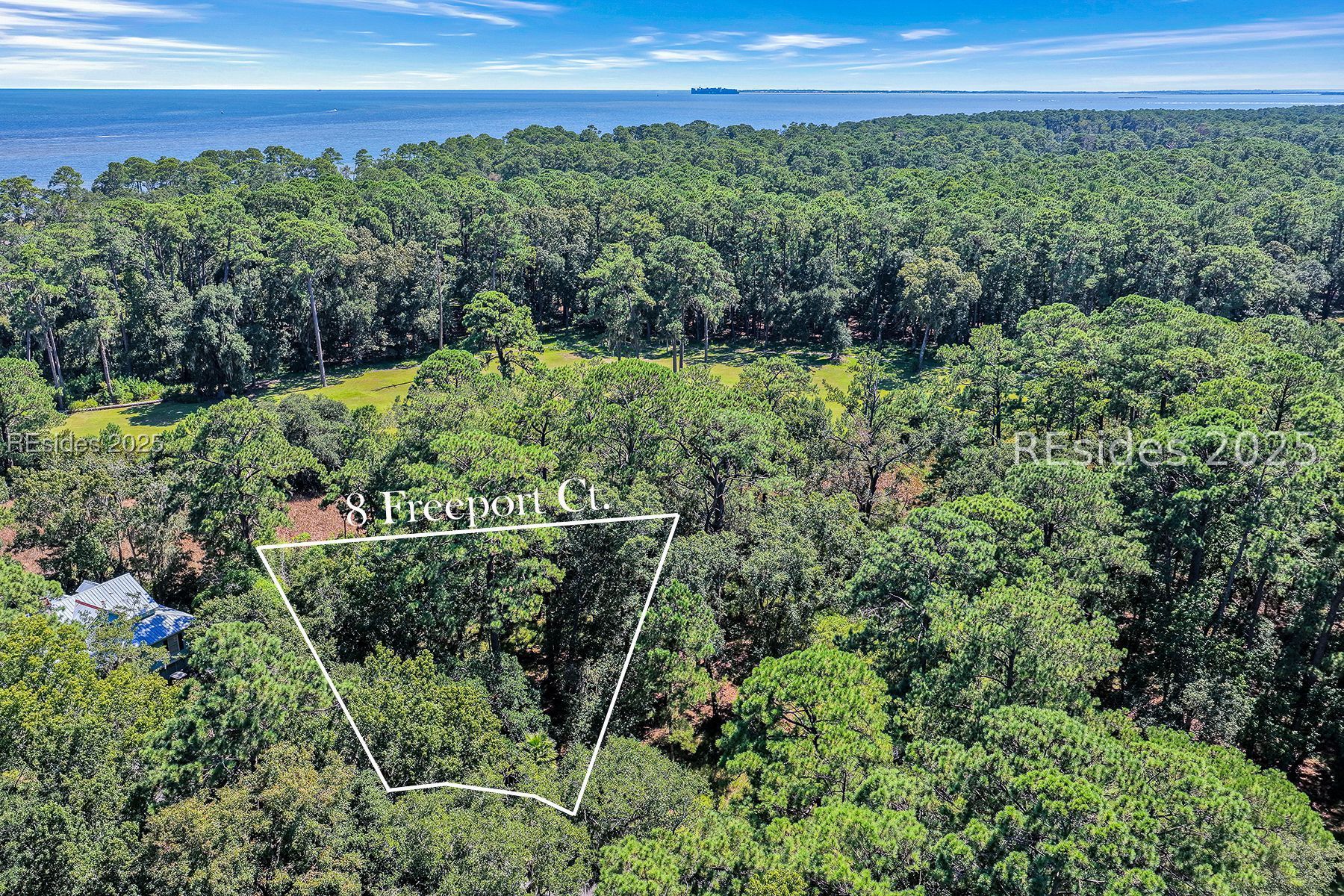 Aerial view of wooded 8 Freeport Court lot outlined in white, with coastal water beyond.