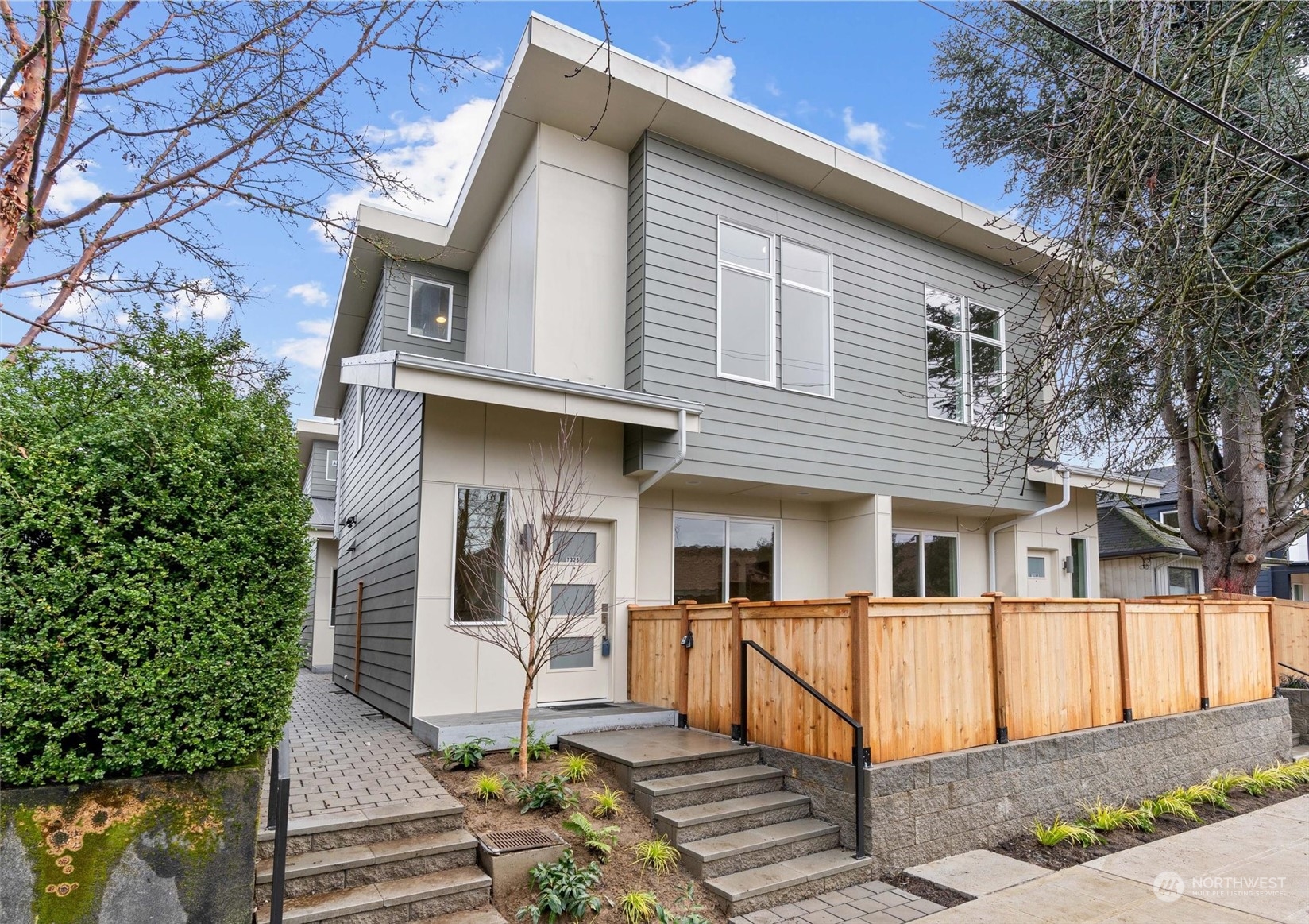 Modern two-story home with gray siding, an angular roofline, and a fenced front patio.