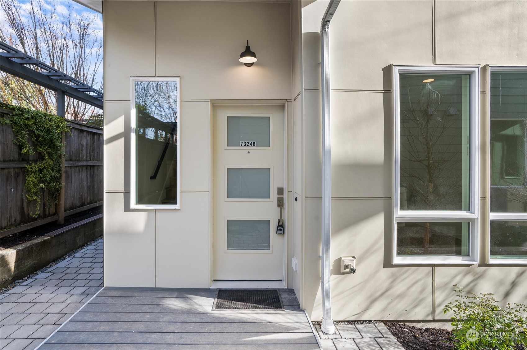 Modern home entrance with a frosted-glass door, large windows, and paved walkway.