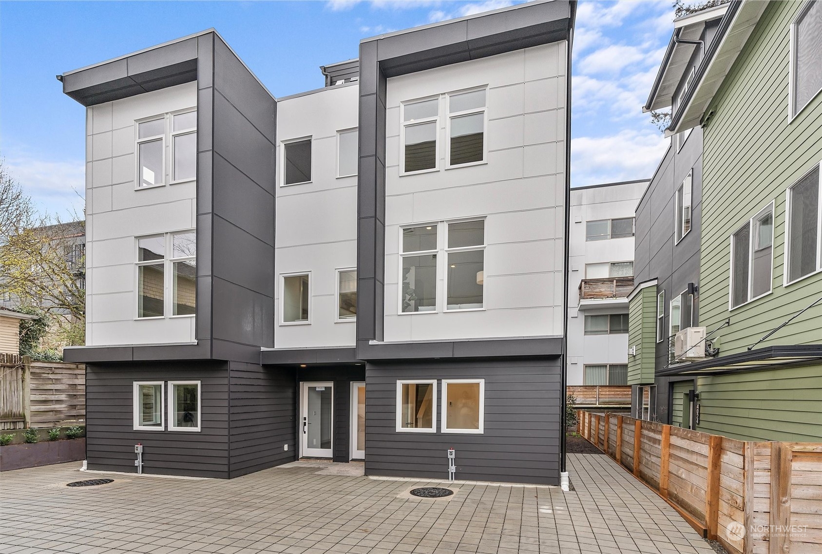 Modern multi-story home with white and charcoal exterior and paved courtyard.