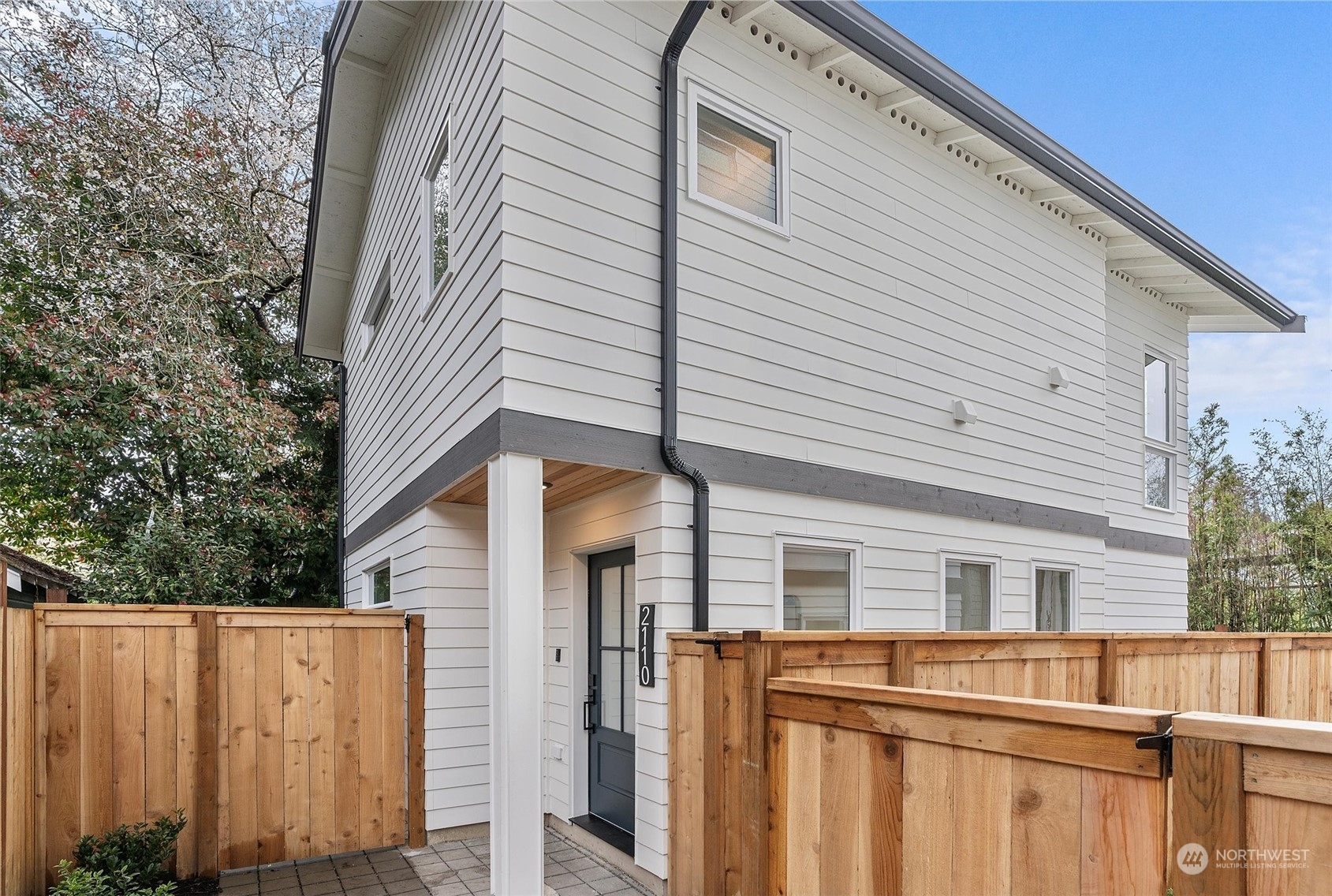 White two-story house with gray trim and a wooden privacy fence around its entry courtyard.