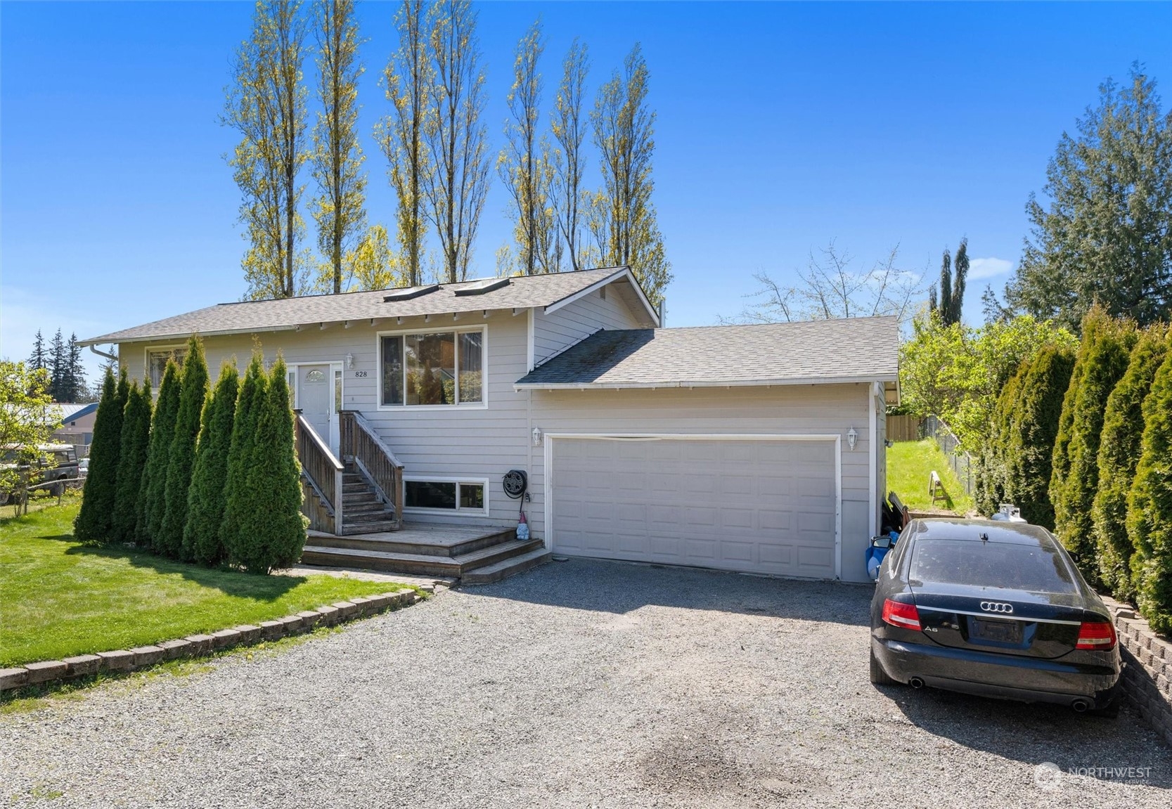 Gray split-level house with a two-car garage, front steps, and a gravel driveway.